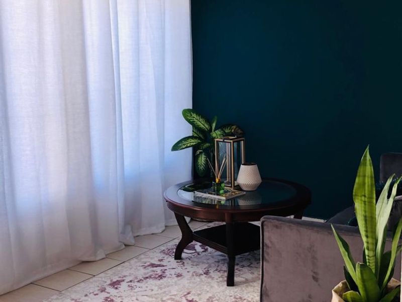 A cozy living room area featuring neutral tiled flooring, a dark accent wall, and natural light filtered through sheer curtains.