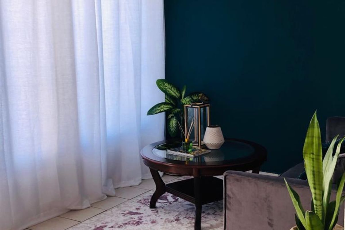 A cozy living room area featuring neutral tiled flooring, a dark accent wall, and natural light filtered through sheer curtains.