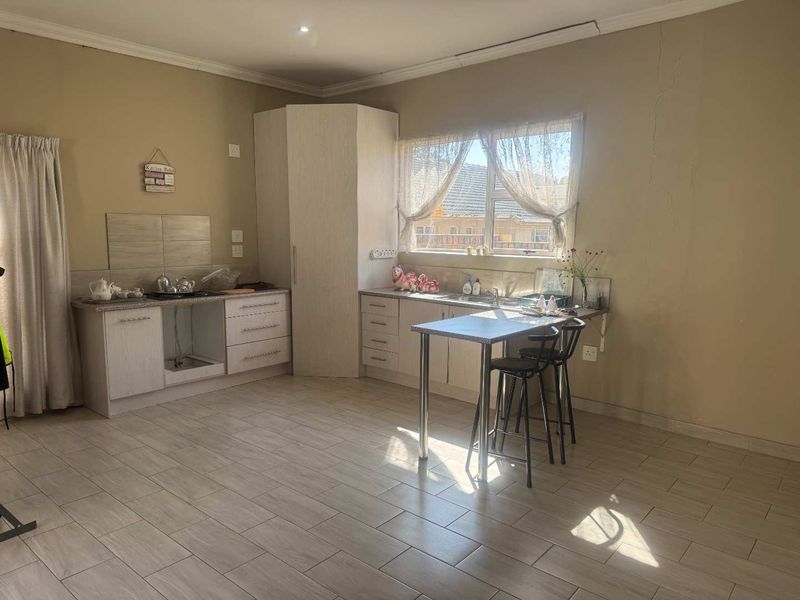 A functional kitchen area featuring light-toned cabinetry, tiled flooring, and a breakfast nook, currently showing signs of wear and wall cracking.