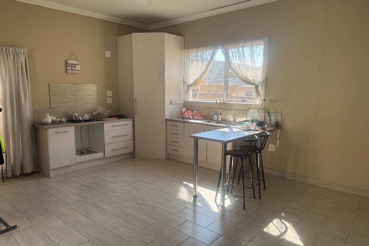 A functional kitchen area featuring light-toned cabinetry, tiled flooring, and a breakfast nook, currently showing signs of wear and wall cracking.