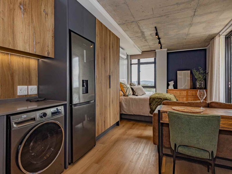Modern open-plan studio apartment featuring an exposed concrete ceiling, sleek wood-grain cabinetry, integrated appliances, and large windows with natural light.