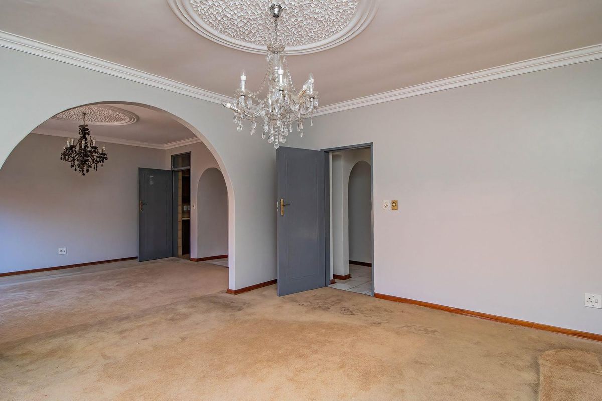 Spacious living area featuring ornate ceiling roses, crystal chandeliers, and classic archways, offering a blank canvas for renovation.