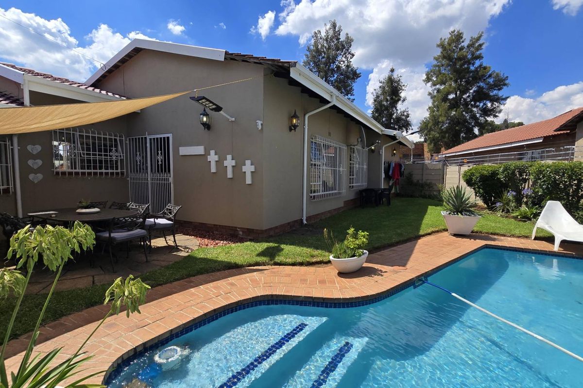 Rear exterior view featuring a swimming pool with brick coping, a paved patio area, and a well-maintained garden space.