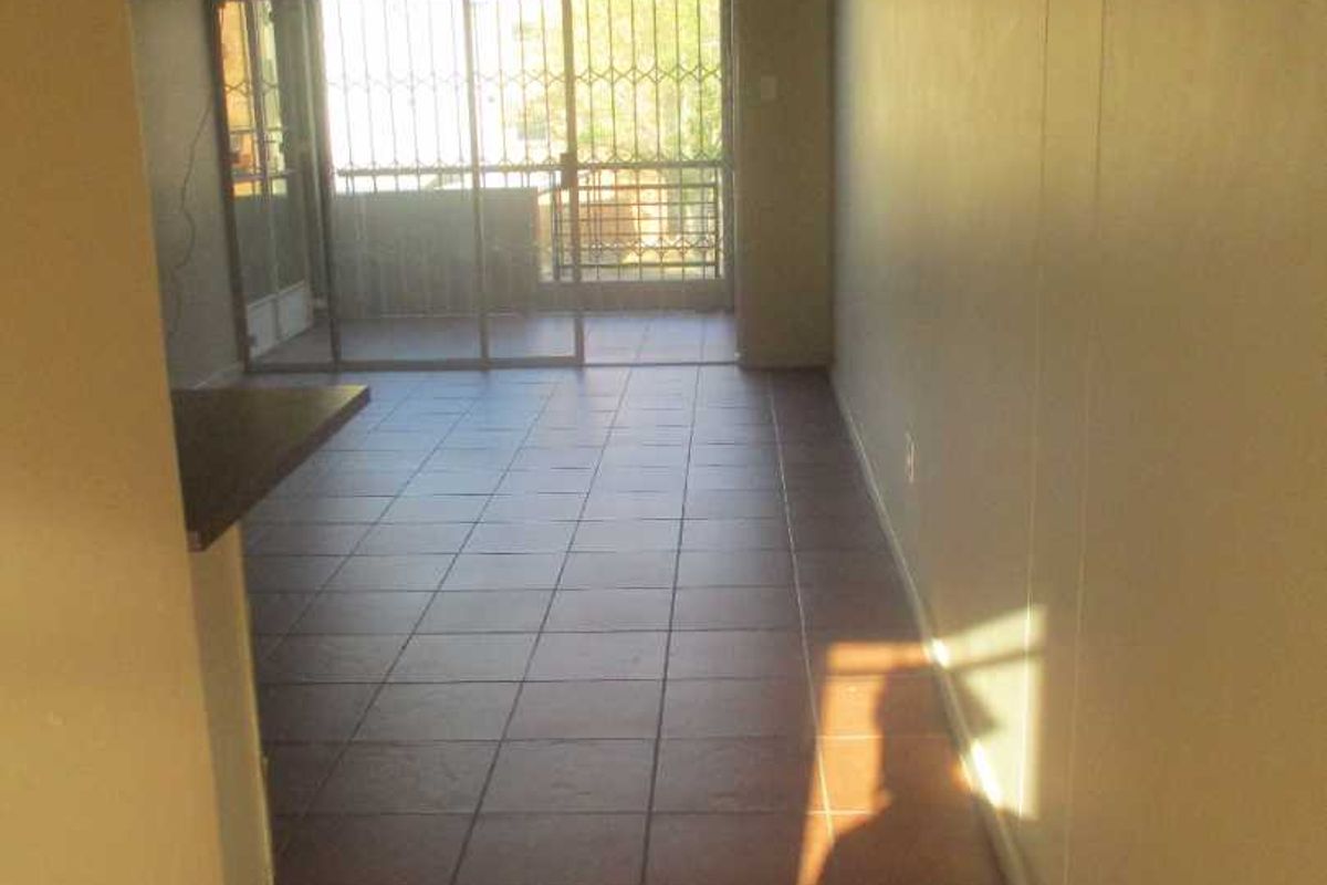 An empty living area featuring tiled flooring and a sliding glass door leading to a balcony, providing access to natural light.
