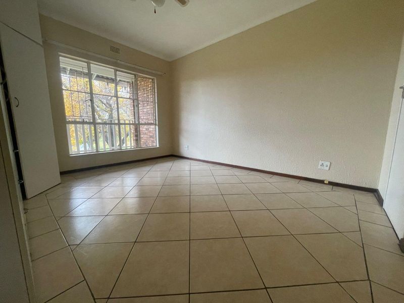 A spacious, empty bedroom featuring neutral tiled flooring, a built-in cupboard, and a large window providing natural light.