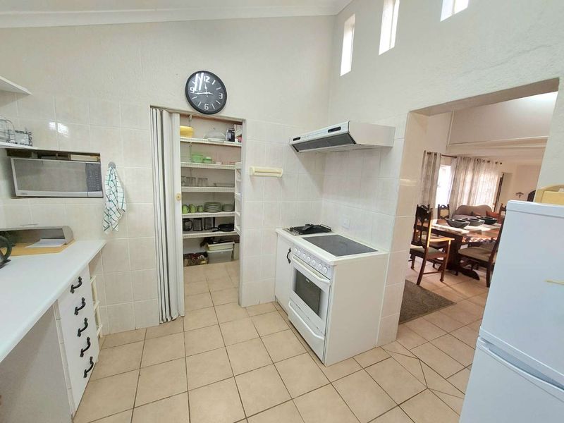 Functional kitchen featuring tiled splashbacks, built-in oven with hob, extractor fan, and a convenient walk-in pantry with shelving.