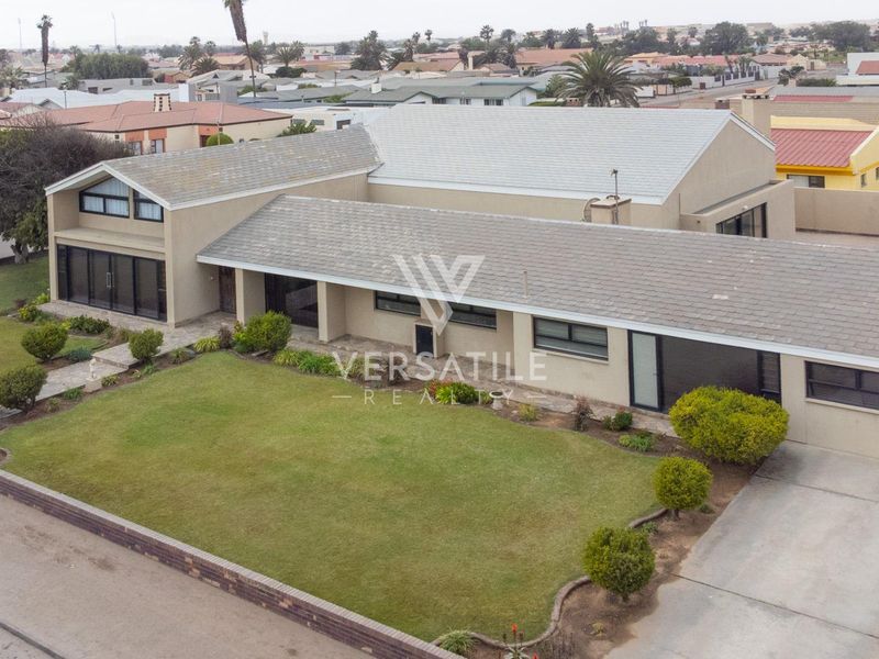 Aerial view of a residential property featuring a large lawn, concrete driveway, and a multi-section tiled roof structure.