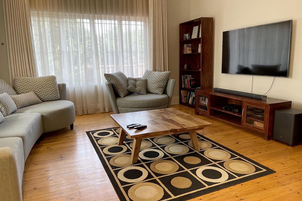 A comfortable living room featuring polished timber flooring and large windows with floor-to-ceiling curtains, providing a bright and inviting space.