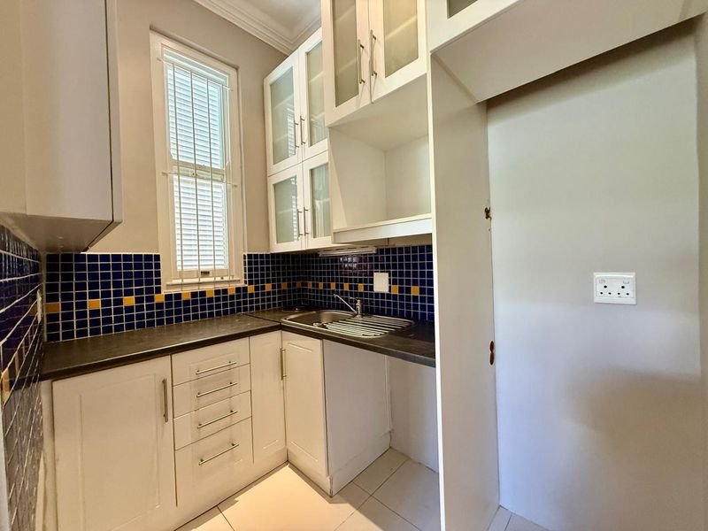 A compact scullery featuring white built-in cabinetry, a stainless steel sink, and a vibrant blue and yellow tiled backsplash.