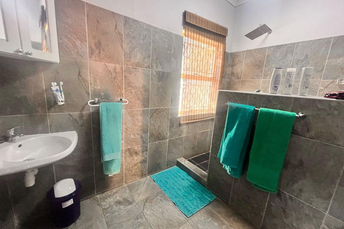 A functional bathroom featuring a walk-in shower with a rainfall shower head, wall-mounted basin, and full-height wall tiling.