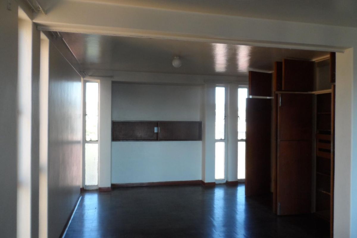 An empty bedroom featuring dark parquet flooring, built-in wooden cupboards, and tall vertical windows providing natural light.
