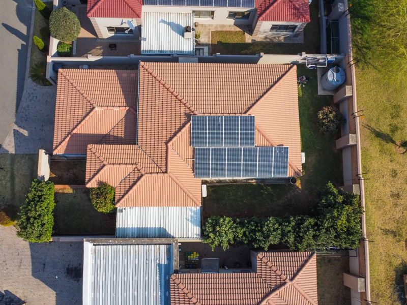 Aerial view of the property showcasing the tiled roof, installed solar panels, surrounding boundary walls, and paved driveway area.