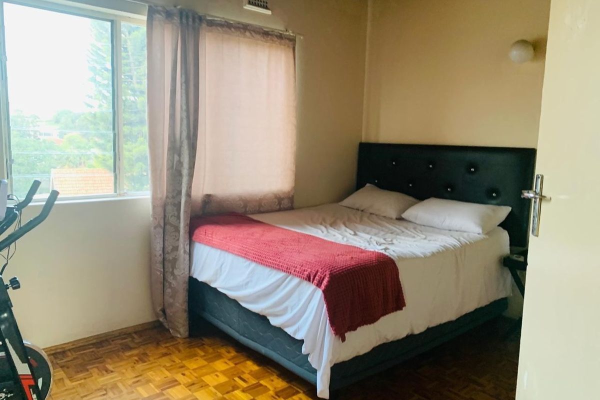A bedroom featuring parquet flooring, a sliding window, and a wall-mounted light fixture, providing a functional and lived-in space.