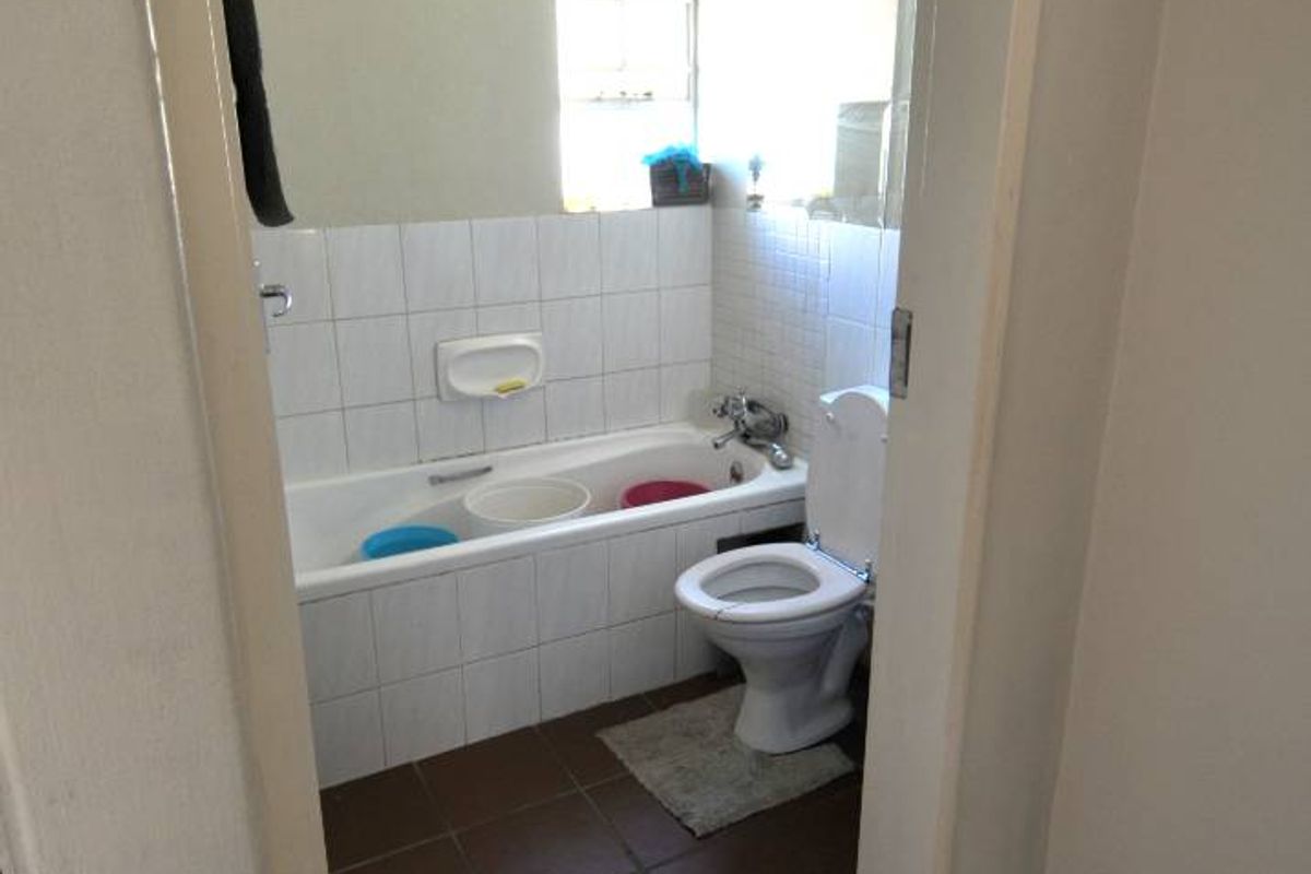A functional bathroom featuring a built-in bathtub, toilet, and tiled flooring, requiring cosmetic updates to modernize the space.