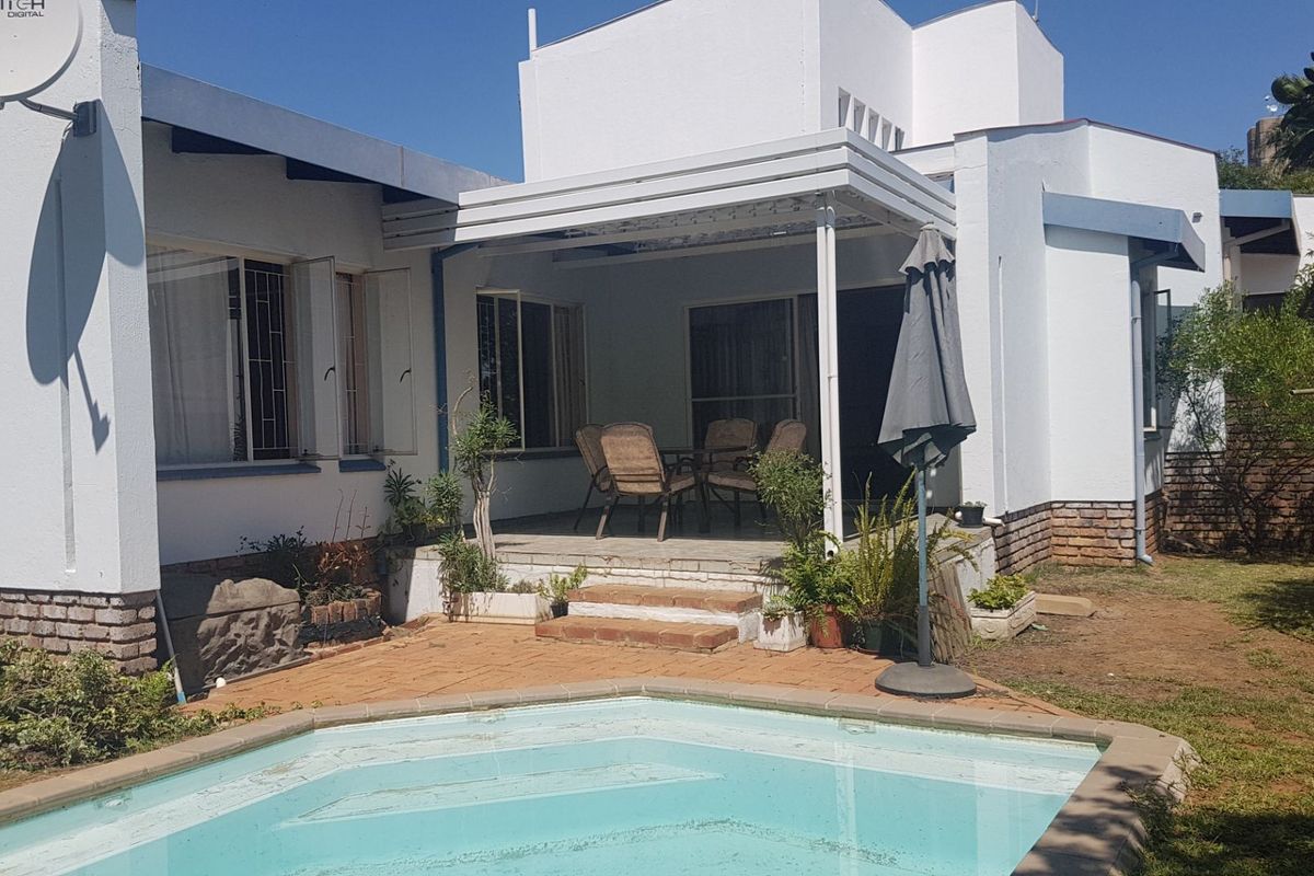 Rear exterior view of the property featuring a swimming pool, paved patio area, and white rendered facade with security bars.