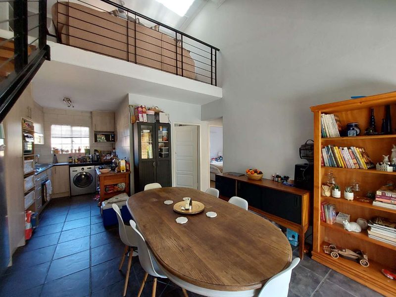 Open plan living and dining area featuring a mezzanine level, tiled flooring, and a functional kitchen space with built-in cabinetry and a skylight.