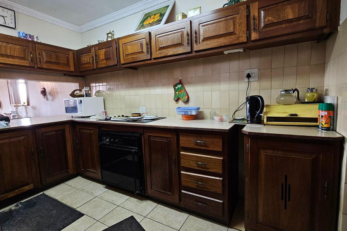 A functional kitchen featuring traditional wooden cabinetry, tiled splashbacks, and built-in oven and hob, offering a classic aesthetic with potential for modernization.