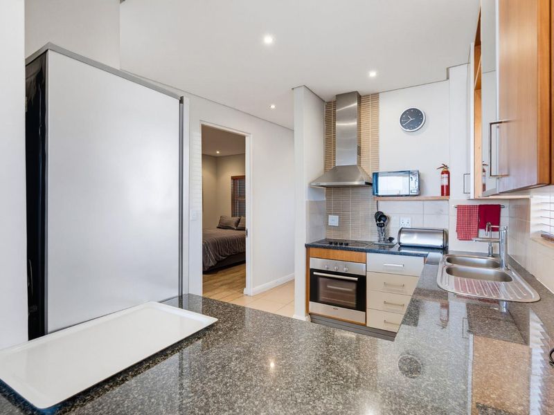 Modern kitchen featuring granite countertops, stainless steel appliances, built-in cabinetry, and a tiled backsplash, with a seamless flow into the adjacent bedroom area.