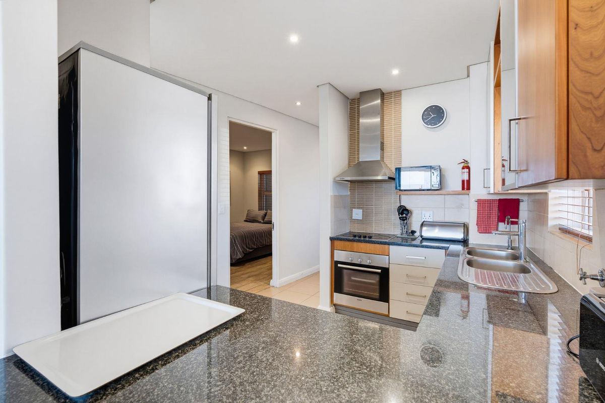 Modern kitchen featuring granite countertops, stainless steel appliances, built-in cabinetry, and a tiled backsplash, with a seamless flow into the adjacent bedroom area.