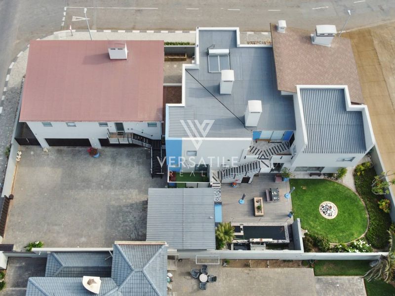 Aerial view of the property showing the main dwelling, paved driveway, swimming pool, wooden decking, and landscaped garden area.