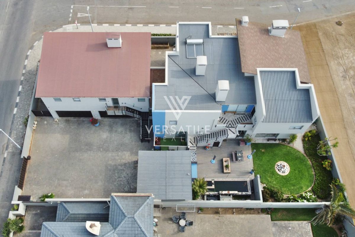 Aerial view of the property showing the main dwelling, paved driveway, swimming pool, wooden decking, and landscaped garden area.