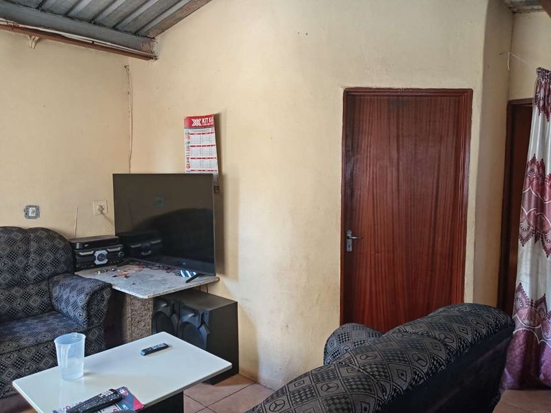 A living room area featuring tiled flooring and a timber door, showing signs of wear on the walls.