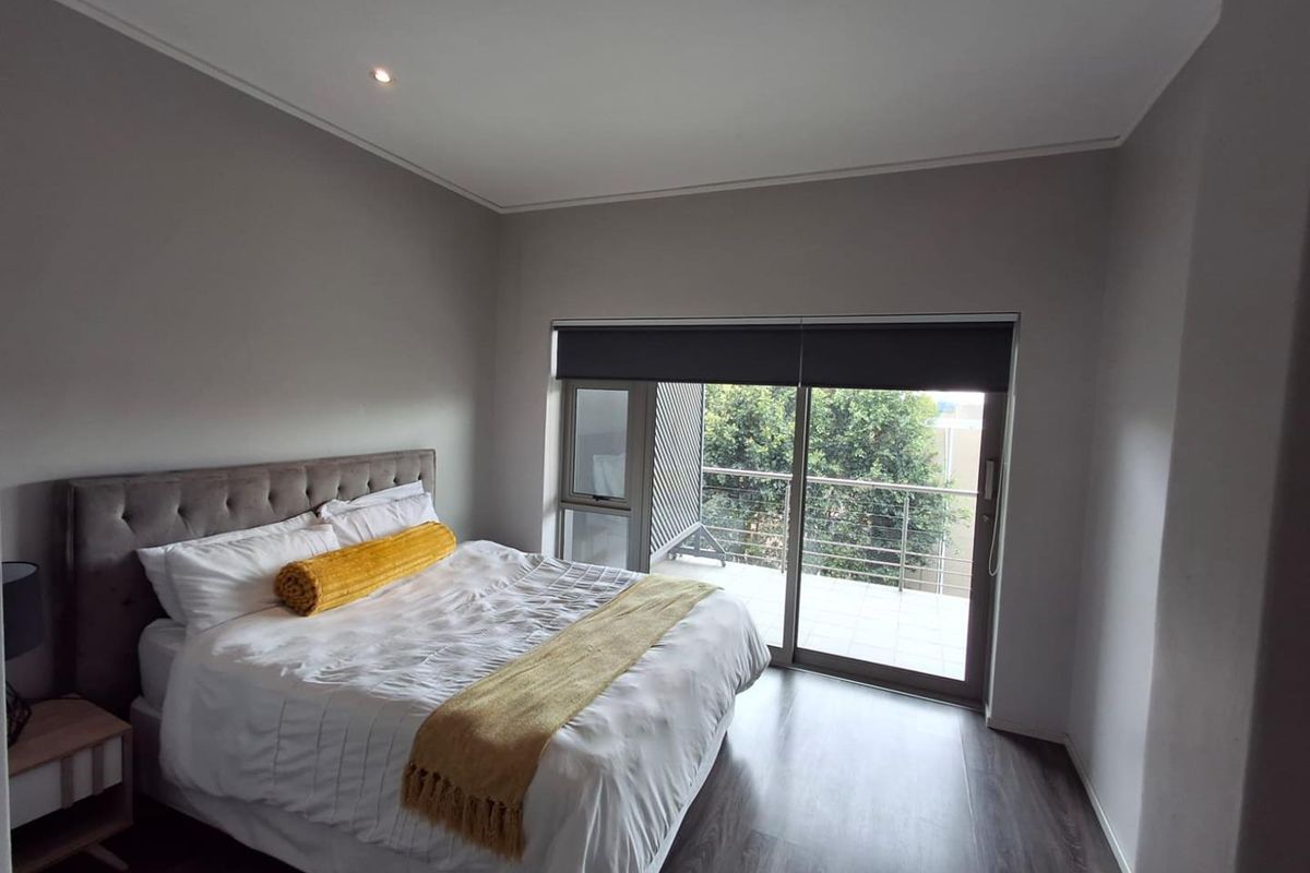 A well-maintained bedroom featuring modern laminate flooring, recessed lighting, and a sliding glass door providing access to a private balcony.