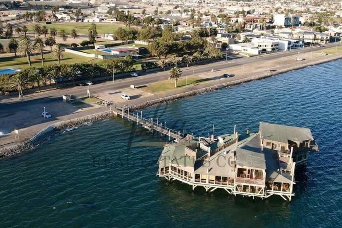 Aerial view of a waterfront commercial property built on stilts over the water, connected to the mainland by a long pedestrian pier.