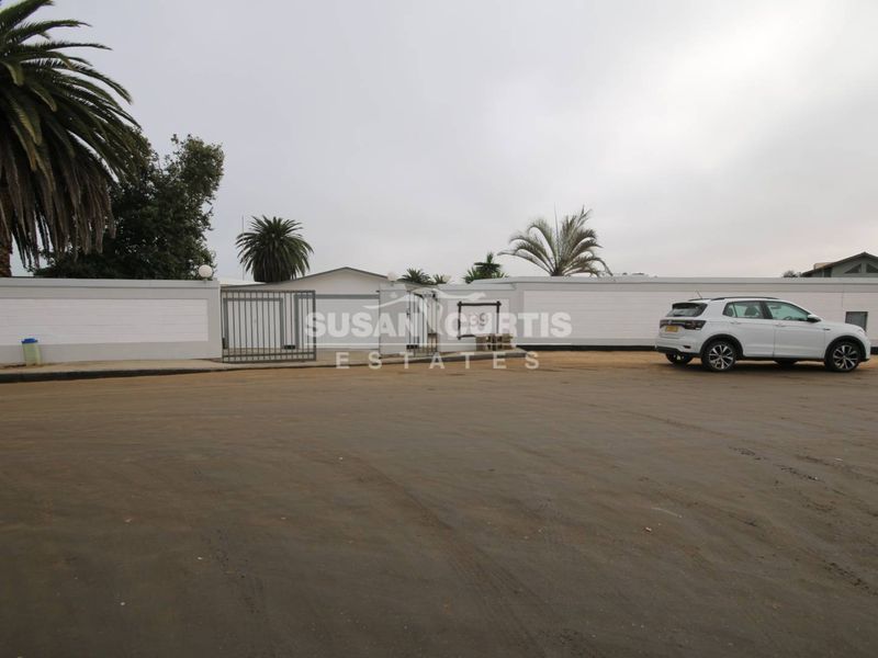 Front exterior view of the property featuring a perimeter wall, gated entrance, and an unpaved driveway area.
