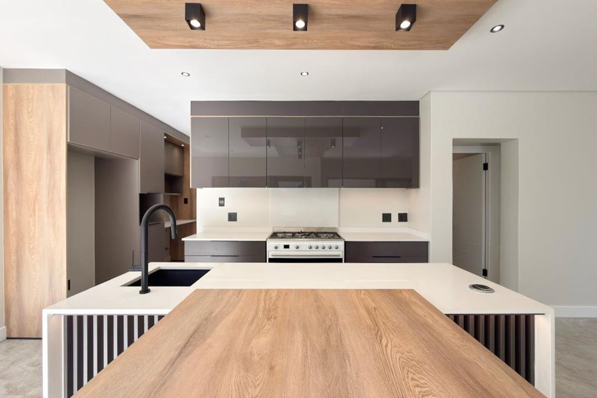 Modern kitchen featuring a central island with a wood-look breakfast bar, integrated cabinetry, stone countertops, and a built-in gas cooktop with extractor.