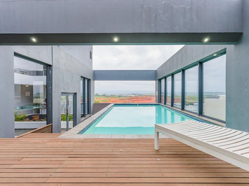A modern rooftop swimming pool area featuring a timber deck, recessed lighting, and expansive views of the surrounding landscape.