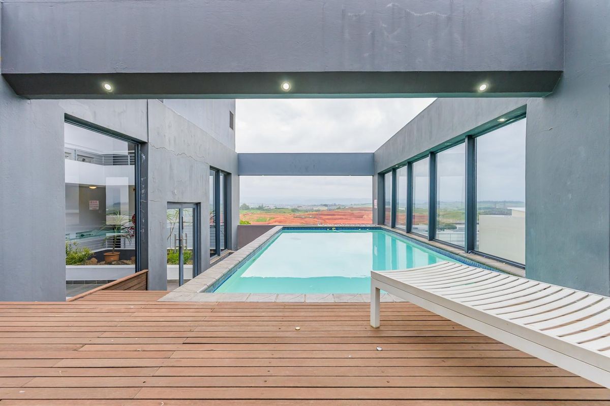 A modern rooftop swimming pool area featuring a timber deck, recessed lighting, and expansive views of the surrounding landscape.