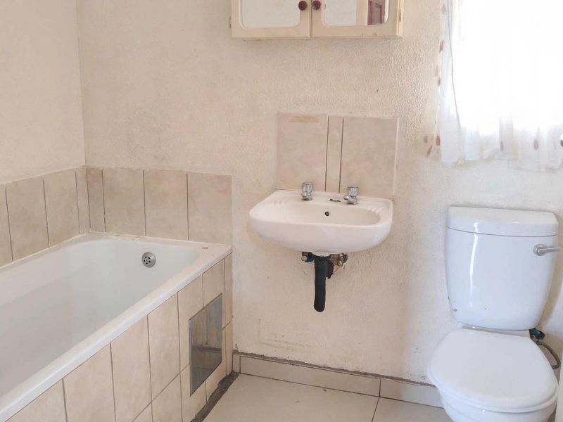 A functional bathroom featuring a bathtub with tiled surround, wall-mounted basin, and toilet, requiring cosmetic updates to improve its overall condition.