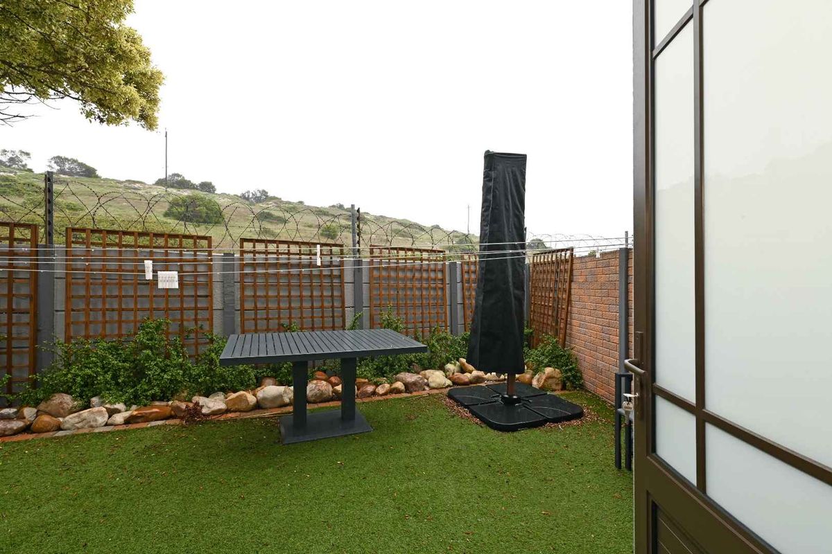 A private rear garden area featuring artificial turf, decorative rock landscaping, and wooden trellis panels against a secure boundary wall.