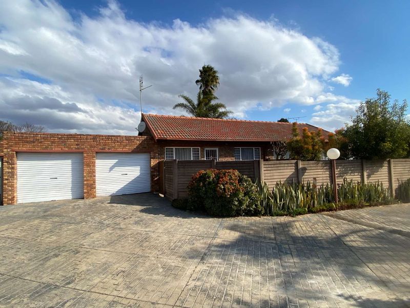 Front view of a townhouse featuring a double garage, paved driveway, and a secure boundary wall with a tiled roof facade.