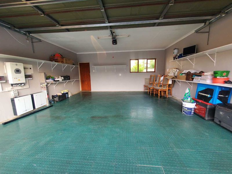 Spacious double garage featuring a sectional door, integrated solar inverter and battery system, wall-mounted shelving, and durable rubber flooring.
