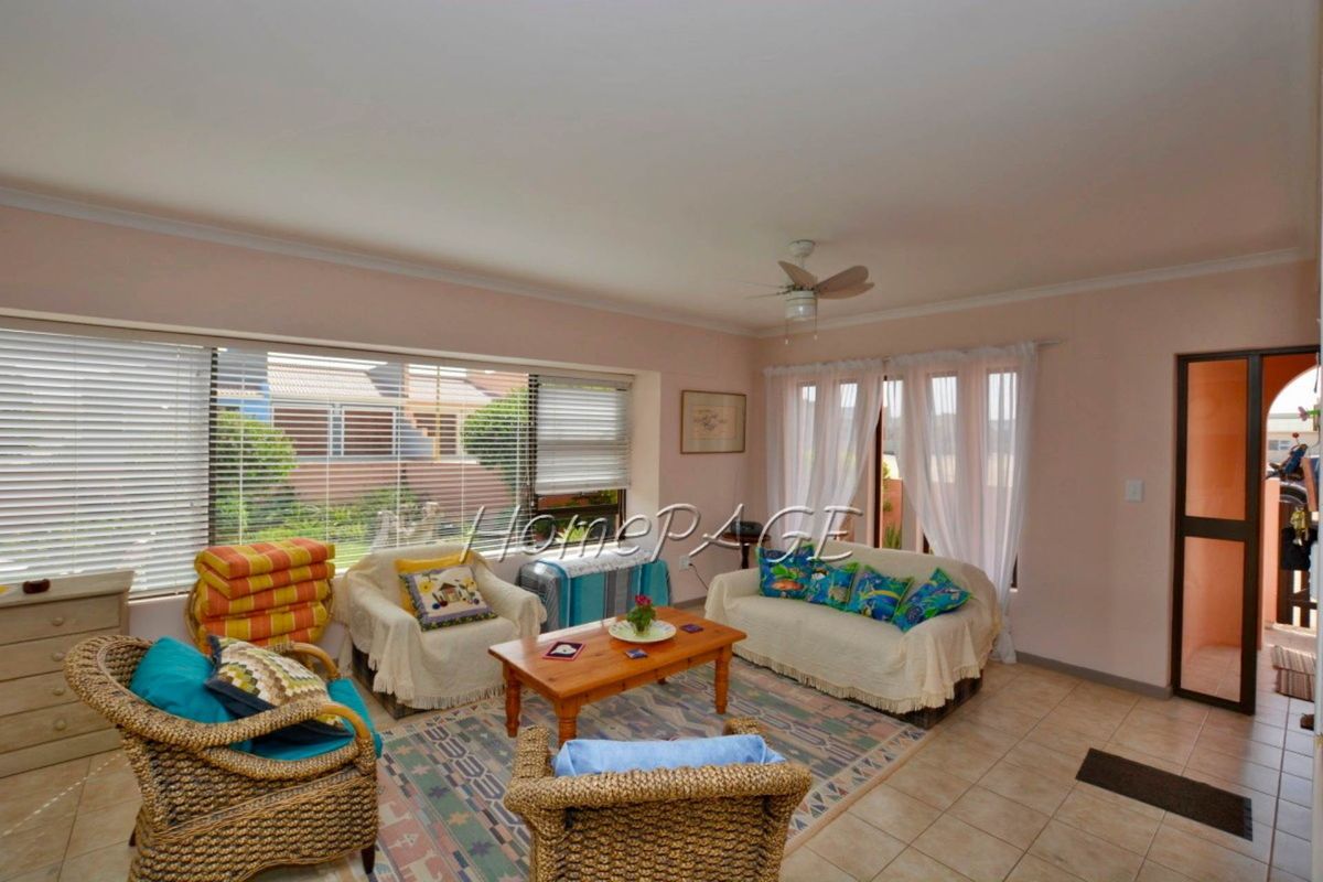 A spacious living room featuring tiled flooring, a ceiling fan, and large windows that provide ample natural light.
