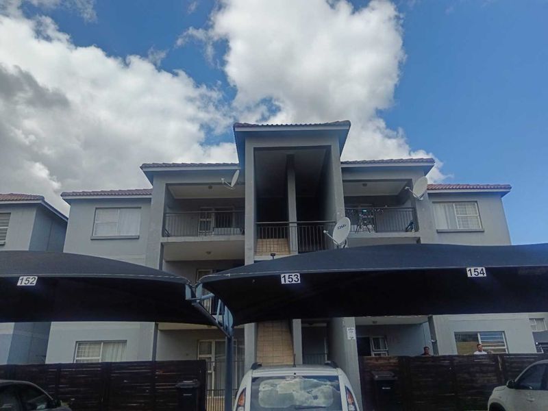 Front elevation of a multi-story apartment complex featuring balconies with metal railings and dedicated shade cloth parking bays.