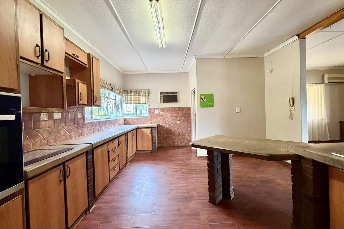 Spacious kitchen featuring wooden cabinetry, built-in oven, and a central breakfast bar, offering a functional layout with potential for modern renovation.