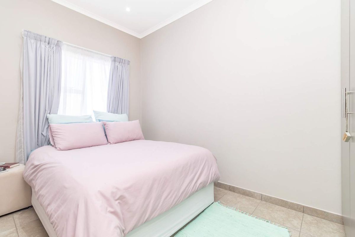 A well-maintained bedroom featuring neutral wall tones, tiled flooring, and built-in cupboard storage.