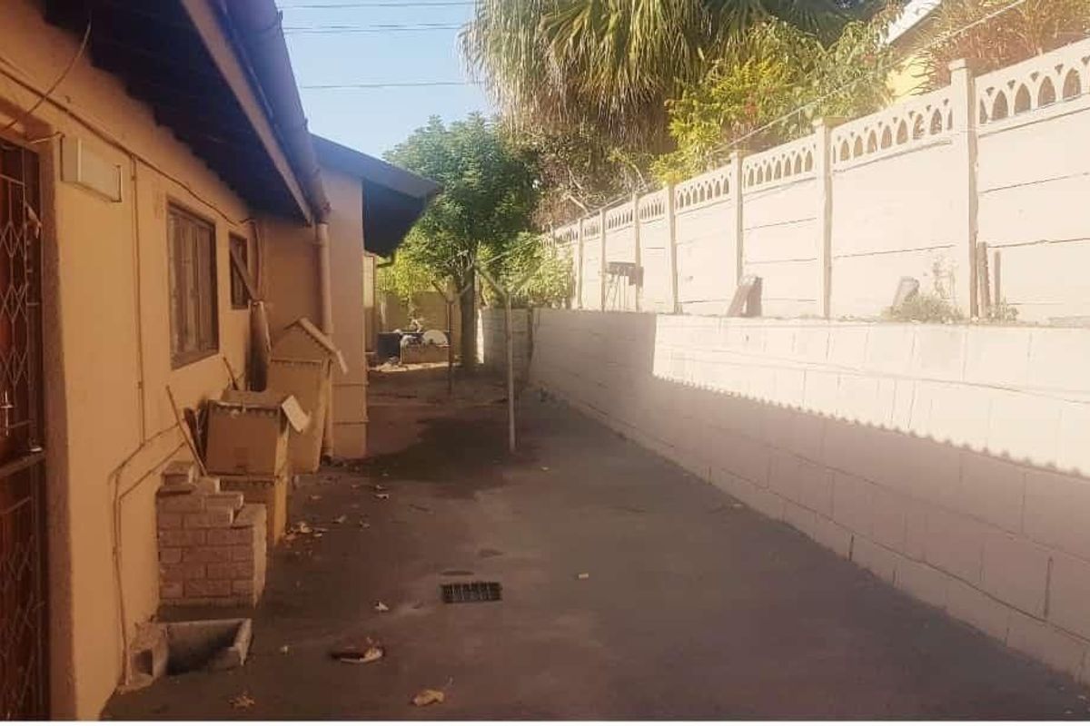 A narrow rear exterior side yard featuring a concrete boundary wall, paved flooring, and a security gate access point.