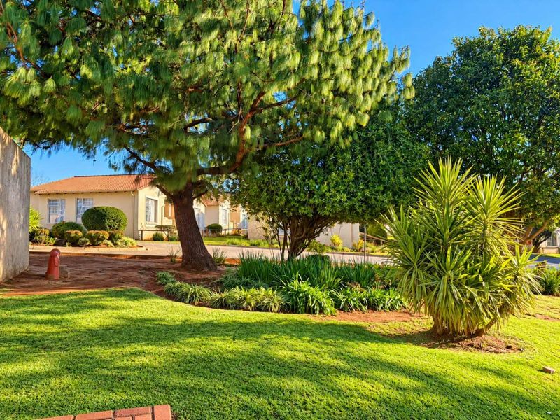 A well-maintained garden area featuring mature trees, lush green lawn, and established landscaping within the townhouse complex grounds.