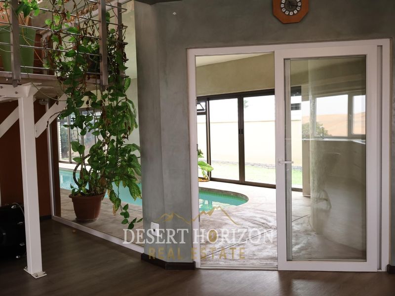 Interior living space featuring a staircase with metal railing and a sliding glass door providing a view of the outdoor pool area.