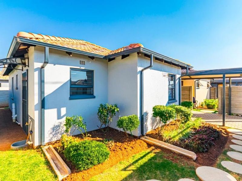 A well-maintained residential exterior featuring a tiled roof, paved driveway, carport, and landscaped garden beds with established shrubs.