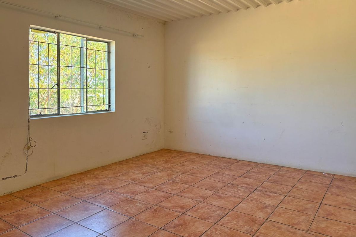 An empty bedroom featuring terracotta-style floor tiles, a window with security bars, and a corrugated metal ceiling.