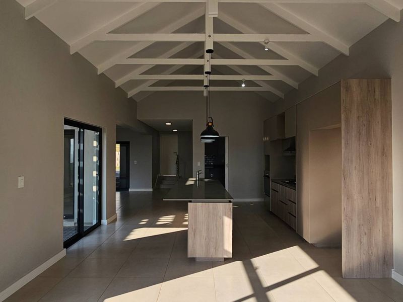Spacious open-plan living and kitchen area featuring vaulted ceilings with exposed trusses, modern cabinetry, a central island, and large windows providing natural light.
