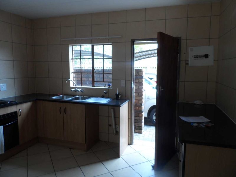 A functional kitchen featuring tiled walls and flooring, granite countertops, a double sink, and a built-in oven, with direct access to the exterior.