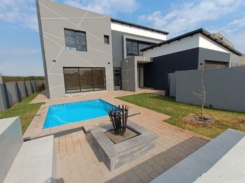 Modern rear exterior featuring a swimming pool, paved patio area with a built-in fire pit, and contemporary architectural facade.