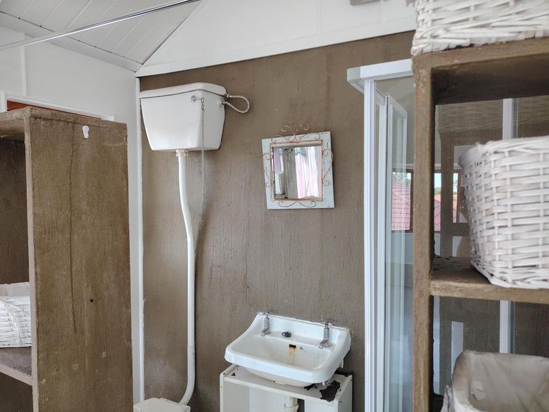 A compact bathroom featuring a vintage high-level cistern toilet, wall-mounted basin, and a shower enclosure with dated finishes.