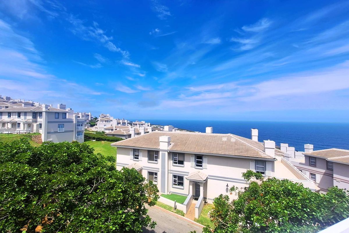 Aerial view of a coastal townhouse complex featuring tiled roofs, chimneys, and well-maintained green spaces overlooking the ocean.